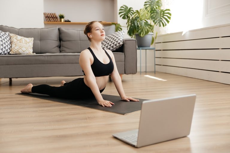 Young attractive woman practicing yoga at homeand uses laptop, yoga for beginners online