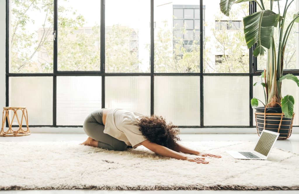 Young mixed race woman practicing yoga balasana pose at home following online classes. Copy space.